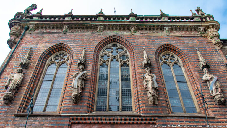 Close view of Bremen Town Hall’s brick façade with tall pointed traceried windows and stone statues between them.