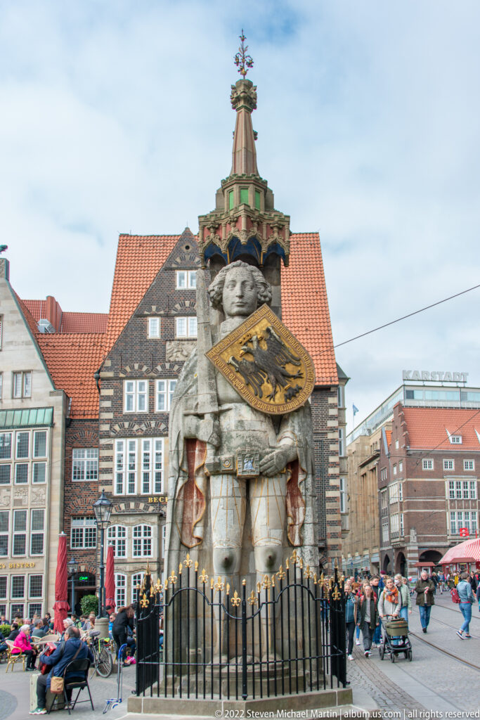 Full view of the Bremen Roland statue beneath its canopy, enclosed by a low iron fence in the market square.