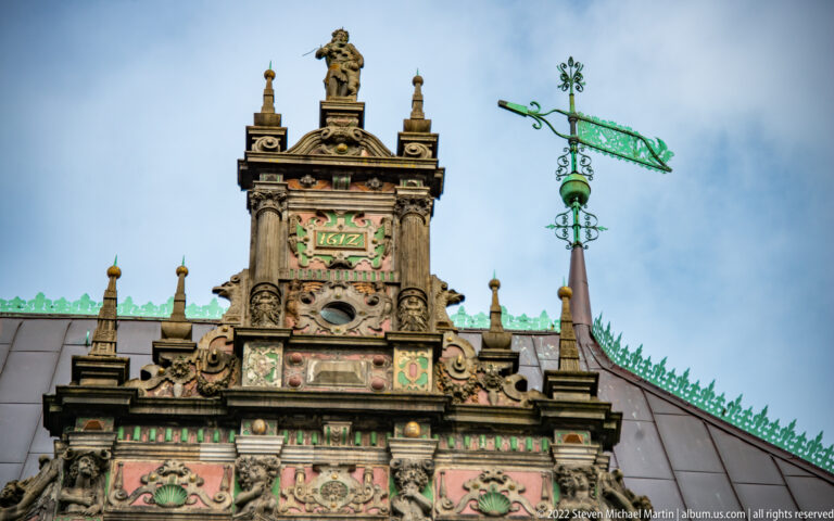 Ornate Bremen Town Hall gable with sculpted figures, colored date panel, and green-patinated weather vane.