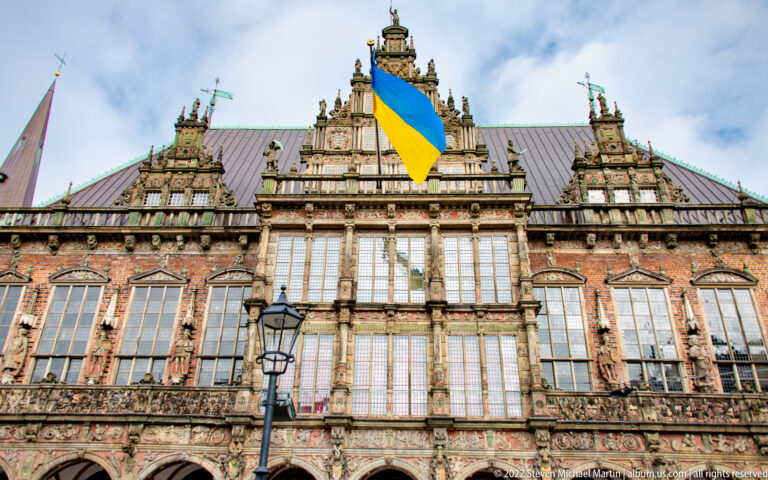 Wide view of Bremen Town Hall’s ornate façade with a large Ukrainian flag hanging from the central gable.