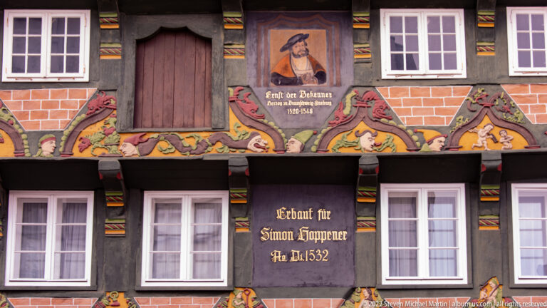 Close view of Hoppener Haus timber façade with painted portrait, carved figures, and inscription “Erbaut für Simon Hoppener Ao 1532.”