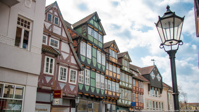 Oblique view of colorful half-timbered houses with projecting upper stories and a black streetlamp in the foreground.