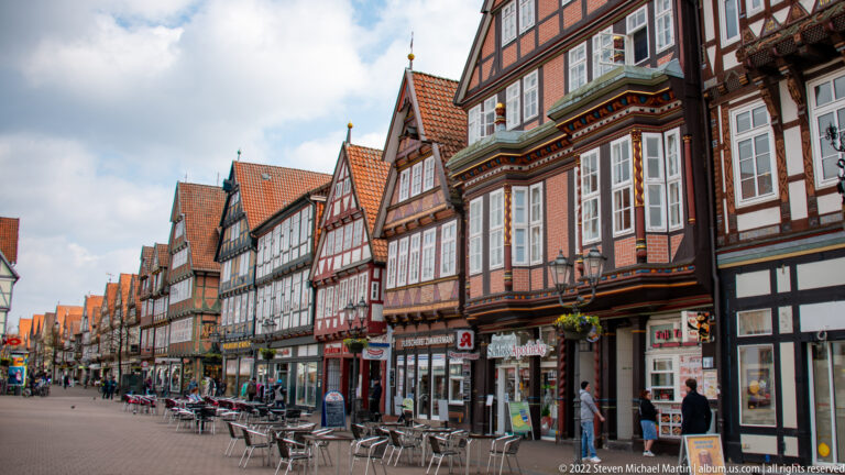 Pedestrian street lined with colorful half-timbered houses, café seating, and shops beneath steep red tile roofs.