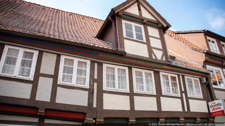 Close view of half-timbered upper story with white windows, small central dormer, and red-brown tiled roof.