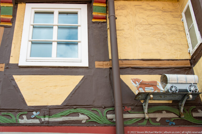 Small relief of a horse pulling a covered wagon mounted on an ochre half-timbered façade above painted floral trim.