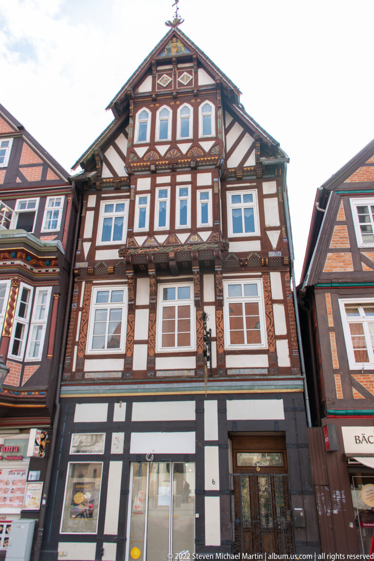 Frontal view of an ornate half-timbered townhouse with dark framing, rows of windows, and a triangular gable.