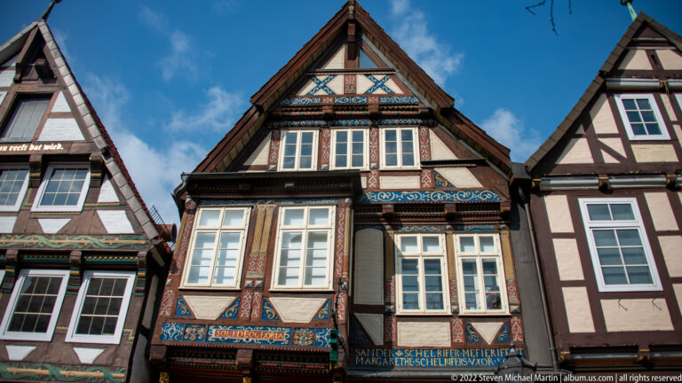 Front view of a steep gabled half-timbered house with painted blue, red, and gold ornament between windows in Celle.