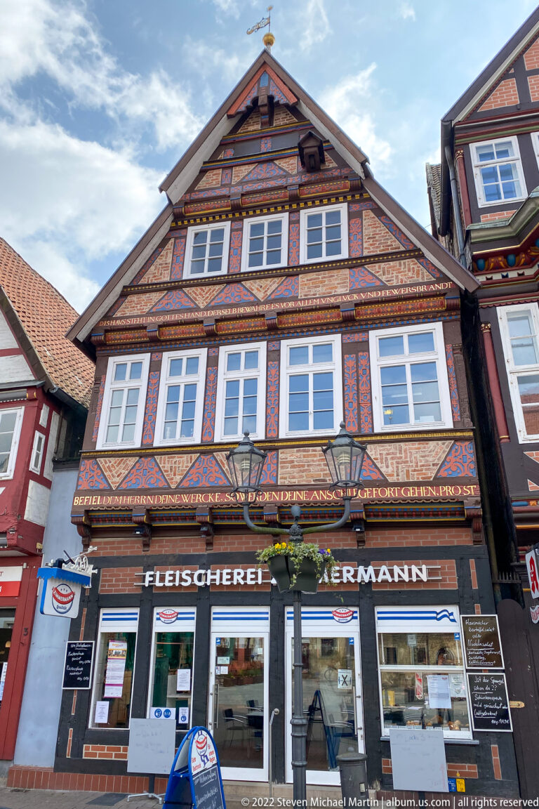 Gabled half-timbered building with ornate painted beams and a ground-floor sign reading “Fleischerei Hermann.”
