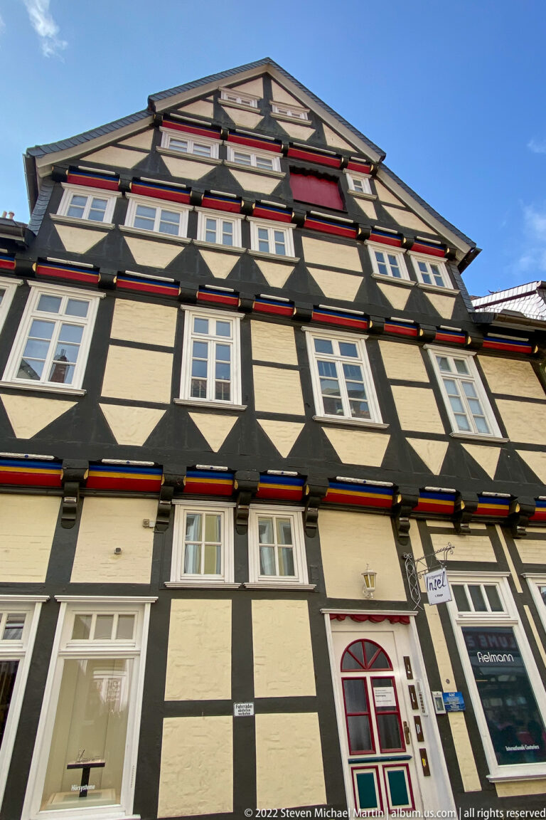 Tall black-and-cream half-timbered townhouse with red trim, white windows, a red-arched doorway, and steep gable.