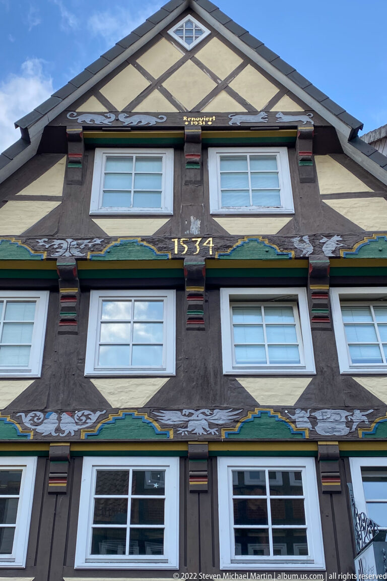 Front view of a dark half-timbered gabled house with pale infill, painted decoration, and the date “1534” on a beam.