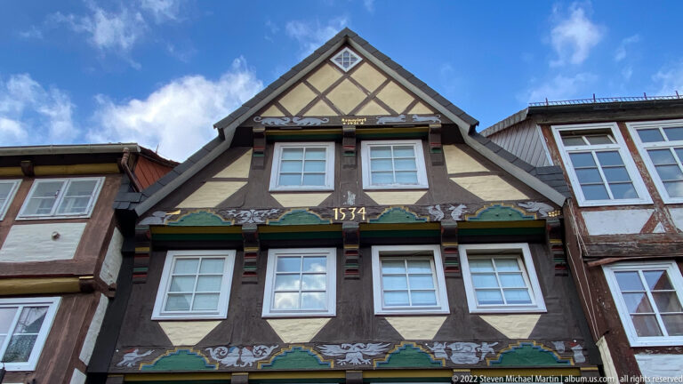 Close frontal view of the upper stories of a half-timbered gabled house marked 1534 with painted decorative bands.