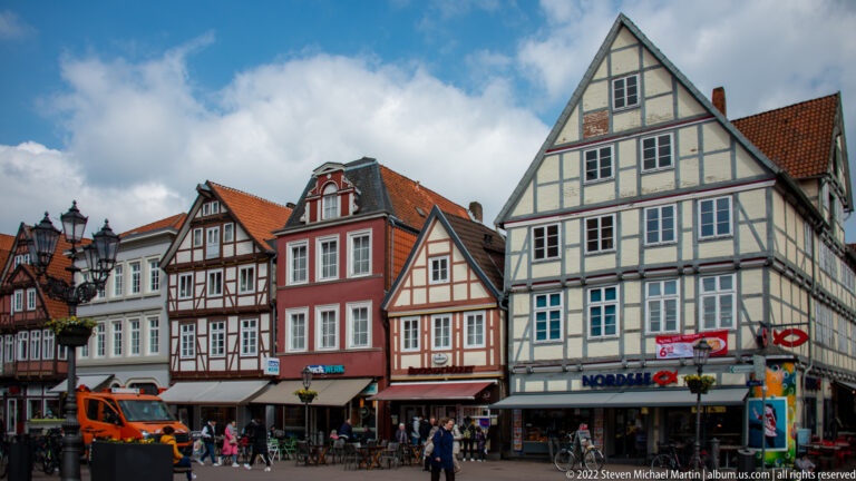 Row of historic gabled houses in Celle, including half-timbered, red stucco, and pale-green façades above shops.