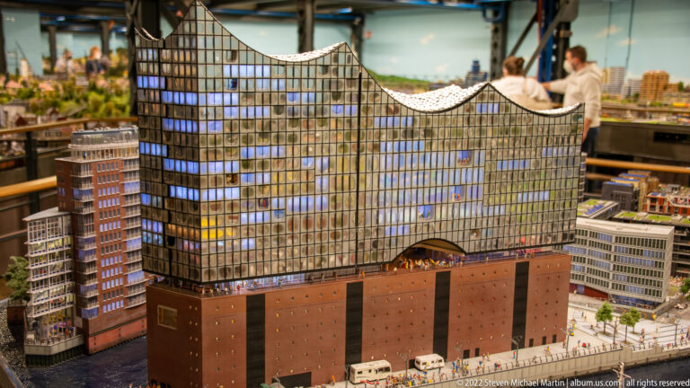 Miniature Elbphilharmonie with glass wave-roofed upper structure above a brick base, surrounded by model city blocks.