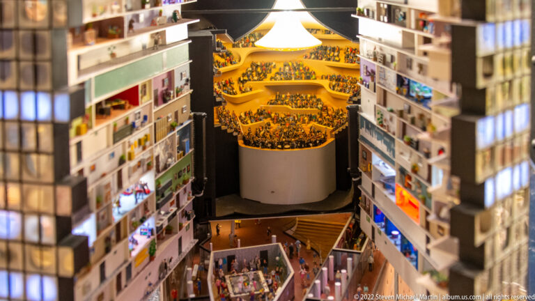 Cutaway miniature of the Elbphilharmonie concert hall with densely seated audience on curved terraced balconies.