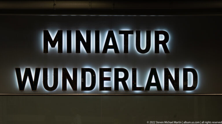 Backlit wall sign reading “MINIATUR WUNDERLAND” in large white letters on a dark background.