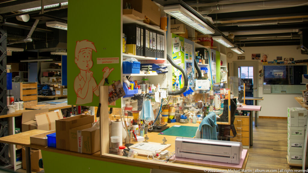 Miniatur Wunderland workshop with workbenches, tools, storage bins, modelmaking materials, and bright task lighting.