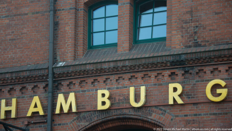 Gold letters spelling “HAMBURG” mounted across a red-brick façade beneath tall arched windows.