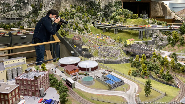 Visitor overlooks miniature mountain landscape with elevated roads, railways, bridges, tunnels, and industrial buildings.
