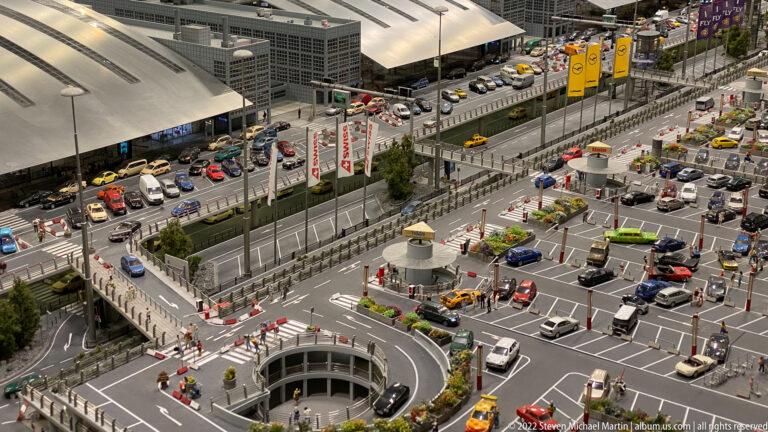 Large miniature multilane intersection crowded with cars, taxis, buses, ramps, crossings, and nearby parking areas.