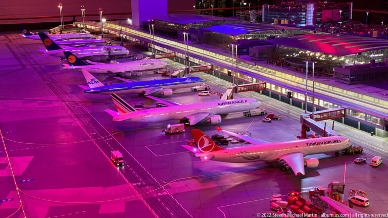 Miniature international passenger jets from Turkish Airlines, Air France, KLM, and Lufthansa parked at terminal gates under magenta lighting.