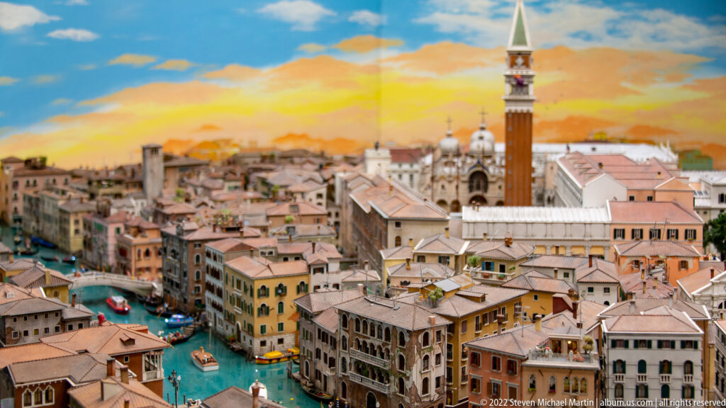 Miniature Venice panorama with St. Mark’s Campanile, basilica domes, canals, bridges, and boats at sunset.