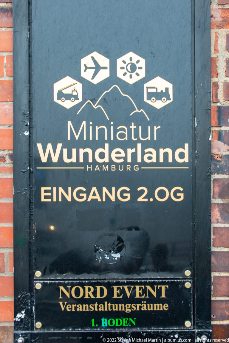 Dark painted sign reading Miniatur Wunderland Hamburg and Eingang 2. OG, with transport icons above.