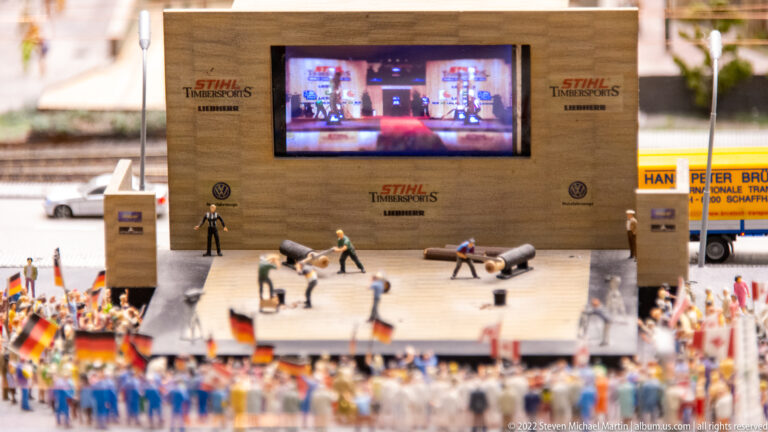 Miniature STIHL Timbersports stage with athletes, officials, large screen, logs, and a packed crowd.