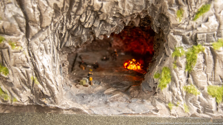 Miniature rocky cavern with a bright orange-red illuminated interior and tiny figures near the entrance.