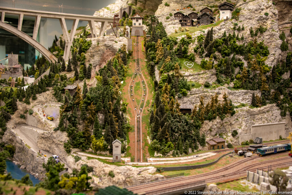 Steep miniature incline railway climbing a rocky mountain, with conventional tracks and a train below.