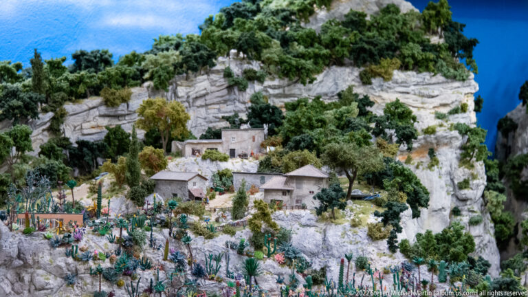 Miniature stone houses clustered among trees and pale cliffs on a steep rocky hillside.