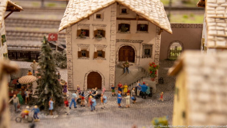 Decorated Swiss alpine house with arched doorway, flower boxes, Swiss flag, and a crowd on the street.