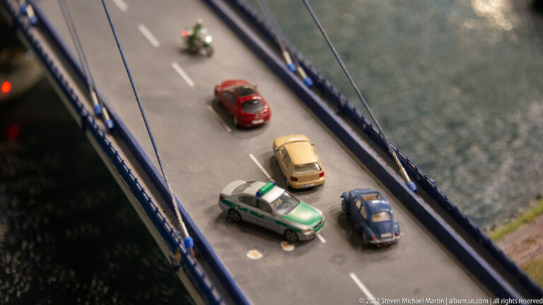 Overhead view of four model cars, including a green-and-white police vehicle, on an elevated road.