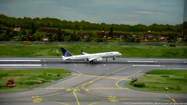 United Airlines model passenger jet taxis on a miniature runway with painted taxiway lines and runway lights.