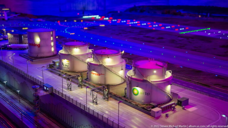 Miniature BP fuel-storage tanks and industrial pipework glow under blue and magenta night lighting.