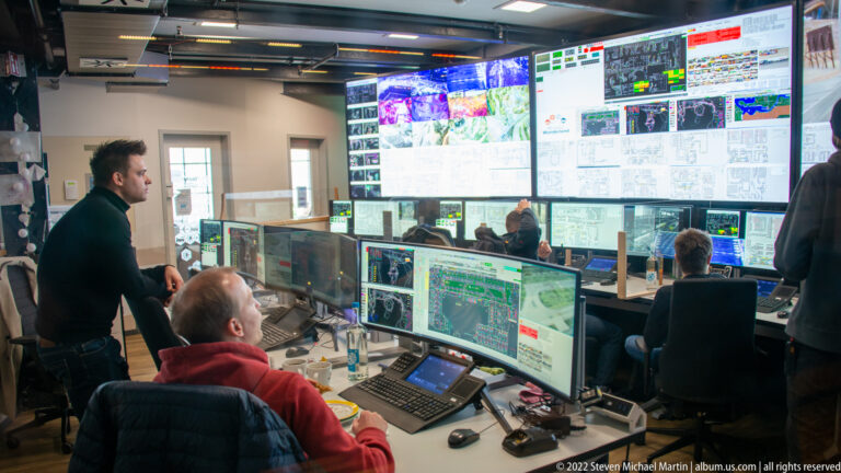 Wide view of Miniatur Wunderland’s control room with staff, desktop monitors, and a wall of system displays.