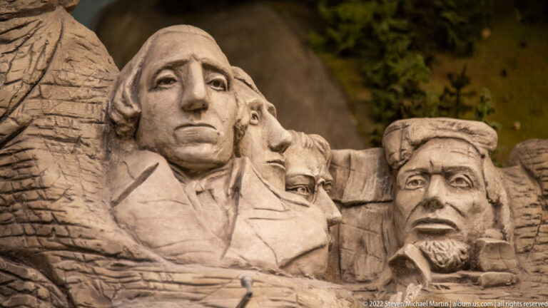 Miniature Mount Rushmore with carved presidential faces modeled in a gray rock cliff.