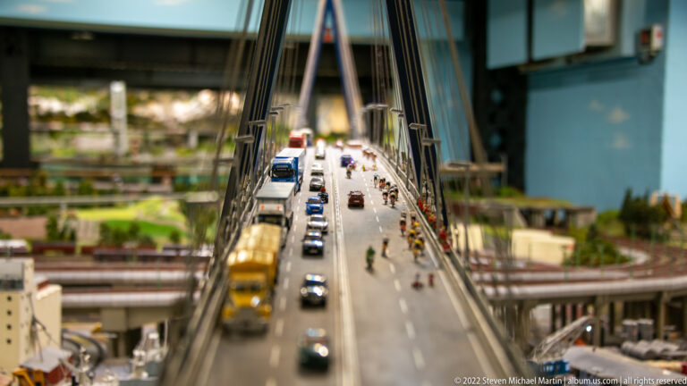 View along a miniature cable-stayed bridge crowded with cars, trucks, motorcycles, cyclists, and pedestrians.