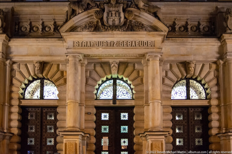 Stone entrance of the Strafjustizgebäude with carved name, columns, arched windows, and heavy doors.