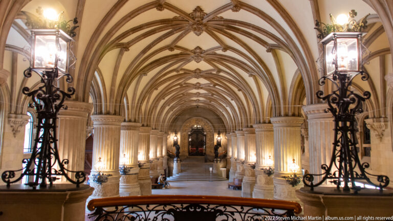 Long Hamburg Rathaus interior gallery with repeated ribbed vaults, stone columns, ornamental lamps, and central aisle.