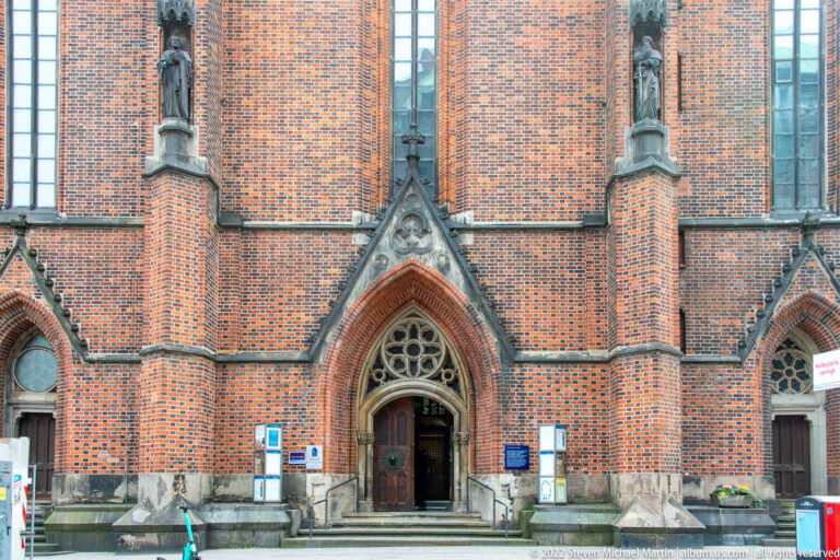 Red-brick Gothic church façade with pointed main doorway, small tracery window, and narrow vertical buttresses.