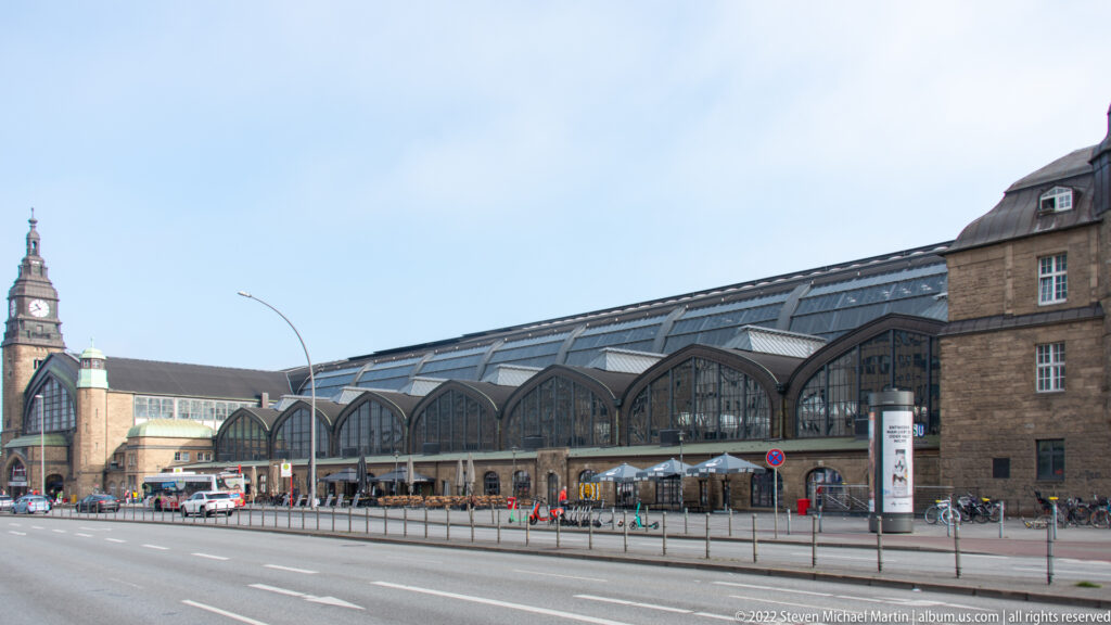 Long arched glass-and-steel façade of Hamburg Hauptbahnhof with street traffic and station tower at left.