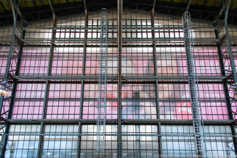 Grid of steel framing, pink-tinted glass, and vertical ladders forming a large wall of Hamburg Hauptbahnhof.