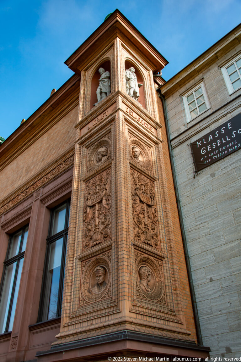 Ornate brick-and-terracotta corner of Hamburger Kunsthalle with portrait medallions, busts, relief panels, and inscriptions.