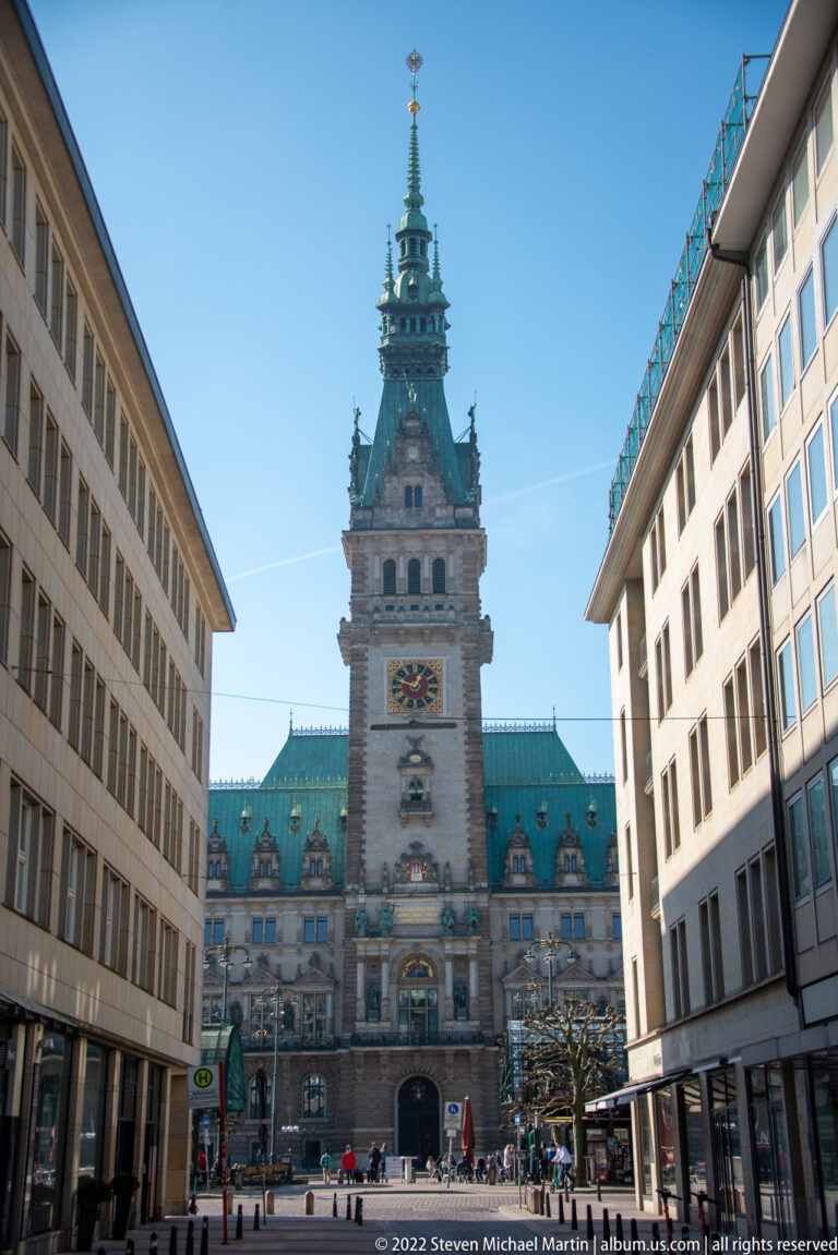 Hamburg Rathaus at the end of a city street, framed symmetrically by modern office buildings.