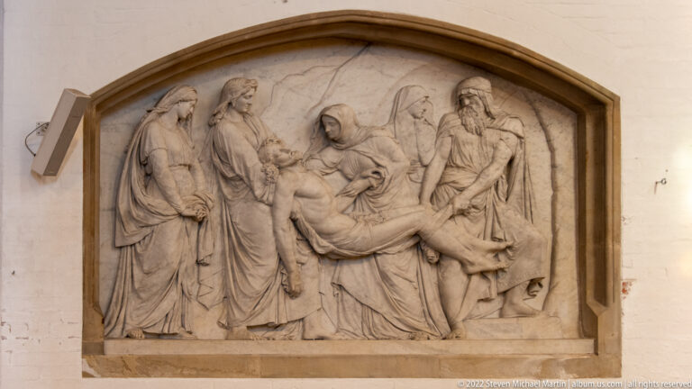 Stone relief of the dead Christ supported by mourners, framed by a shallow pointed arch.