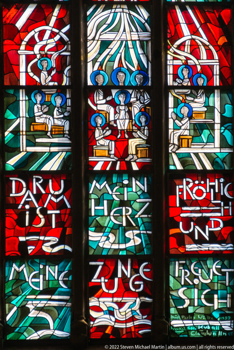 Three stained-glass panels with stylized worshippers, sweeping colored bands, and large fragments of lettering.