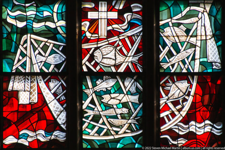 Stained-glass panels with fish, interlaced lines, waves, and a cross in red, green, white, and black.