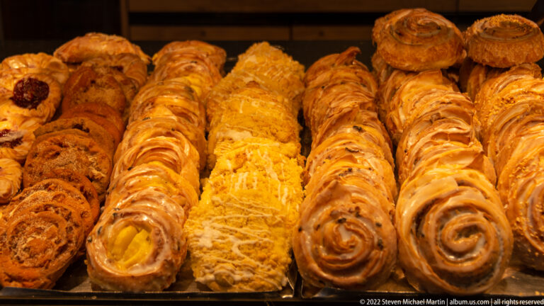 Close-up of rows of golden spiral, glazed, and filled pastries arranged tightly in a bakery display.