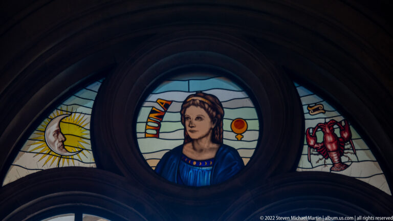 Stained-glass female figure labeled “LUNA,” flanked by crescent moon and red zodiac-like symbol.