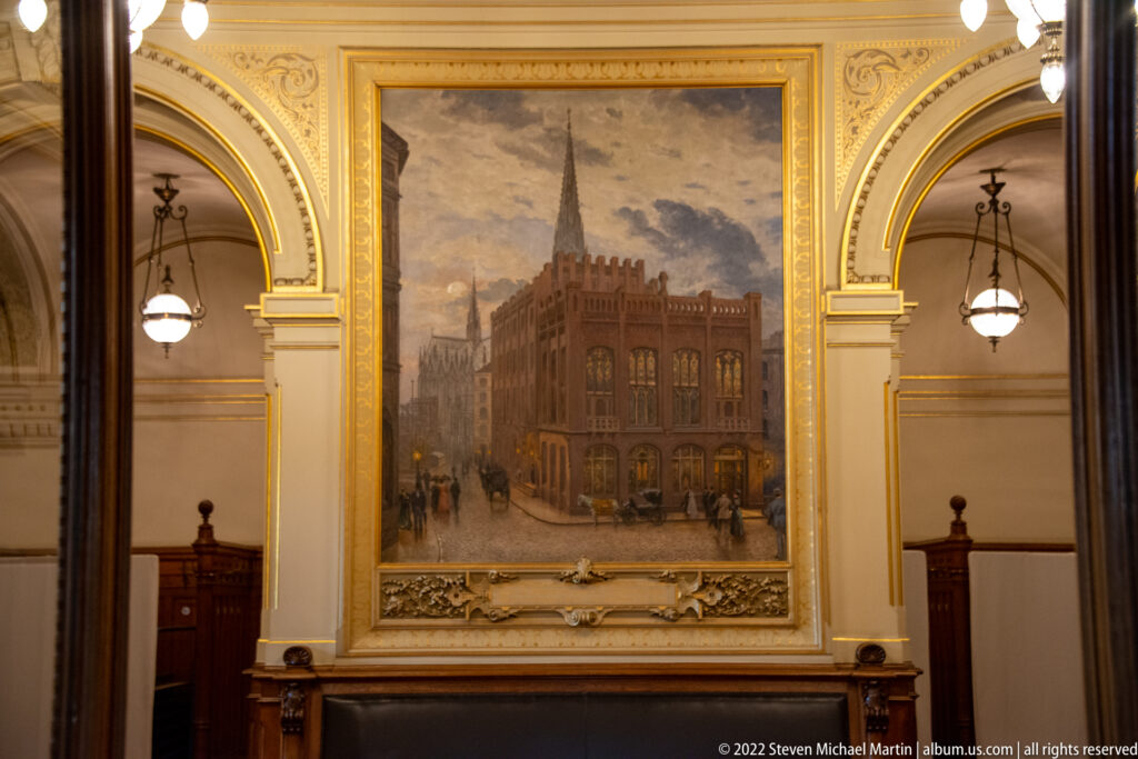 Large framed painting of a historic civic building and square set between gilded arches inside Hamburg Rathaus.